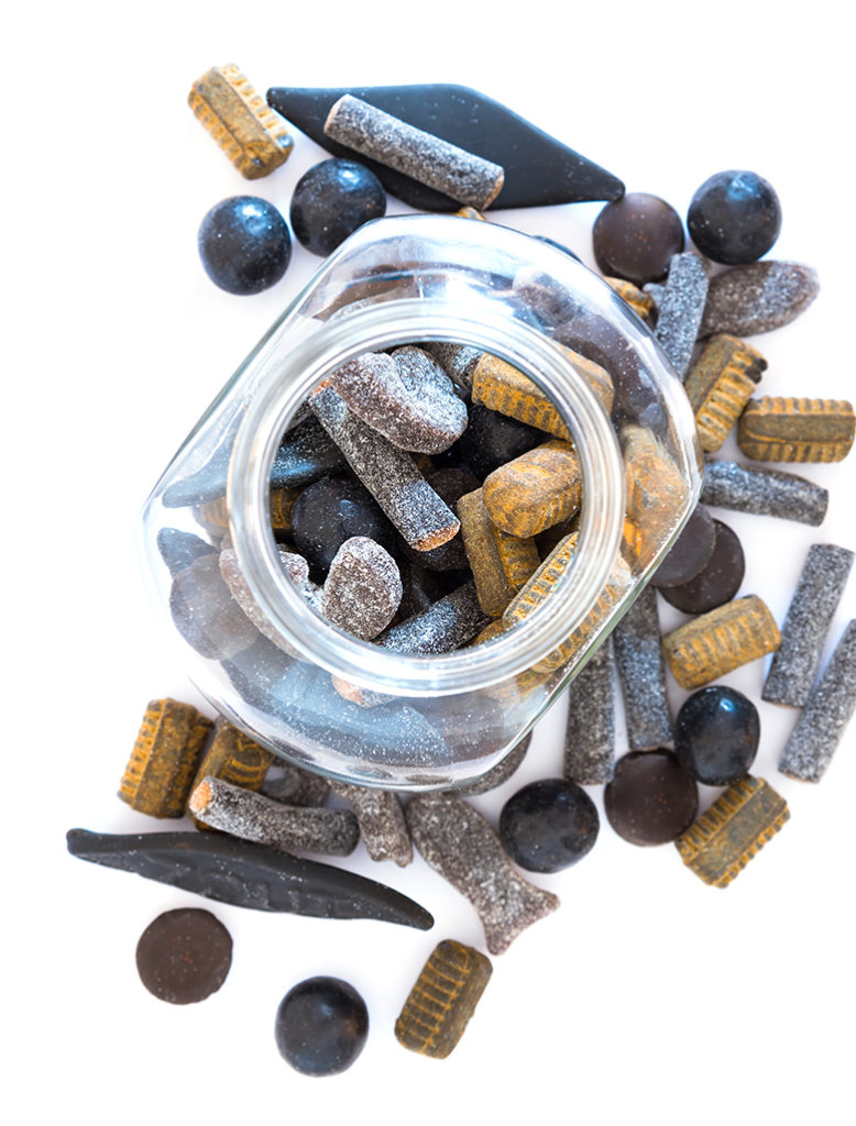 Different varieties of double salted licorice in open glass jar and on white background